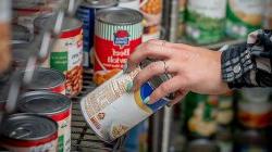 a hand grabbing a can of food off the shelf